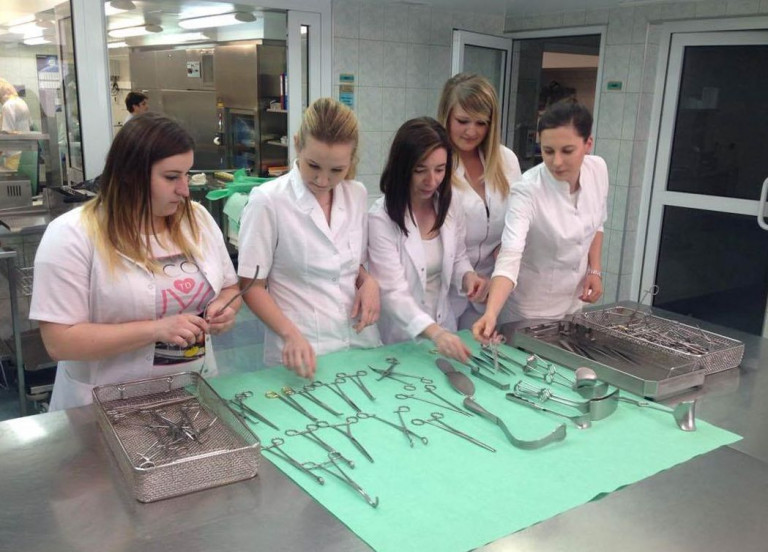 Pięć Kobiet, Uczennic Zawodu Technik Sterylizacji Przy Stole Na Którym Są Rozłozone Narzędzia Chirurgiczne.