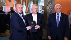 Marszałek Andrzej Bętkowski i członek Zarządu Województwa Marek Jońca gratulują mężczyźnie w granatowym garniturze i koszuli w biało-niebieską kratkę
