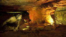Kolorowa rzeźba człowieka pracującego w bardzo niskim korytarzu pod ziemią. Fragment trasy rezerwatu Krzemionki