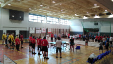 Wnętrze hali sportowej. Zawodnicy stoją obok stołów do gry w tenisa stołego