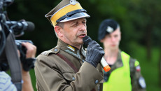 Zdjęcie zbliżenie. Dionizy Krawczyński Komendant Marszu z mikrofonem przemawia. W tle młody żołnierz Wojsk Obrony Terytorialnej
