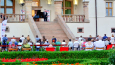 Publiczność siedzi na krzesełkach podczas koncertu w Ogrodzie Włoskim. Artysta muzyk grający na fortepianie stoi obok instrumentu