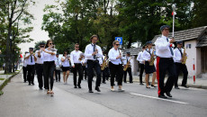 Grupa osób ubranych na biało czarno, w rękach trzymają instrumenty muzyczne. Kielce, maszerując ulicą Jana Pawła Drugiego gra Orkiestra Marszałkowska