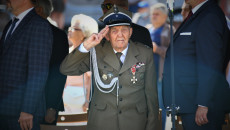 Starszy mężczyzna stoi na baczność wśród oficjeli. Ubrany w mundur z przypiętymi odznaczeniami Kombatant, salutuje zwrócony w stronę fotografa