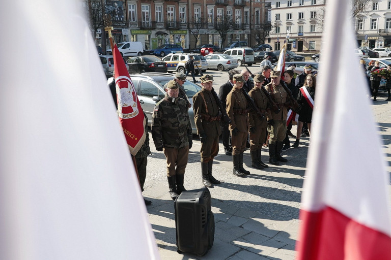 Uczestnicy Uroczystości Pod Pomnikiem, W Tle Flagi Polskie