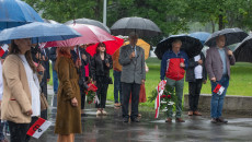 Uczestnicy wydarzenia stoją pod parasolami