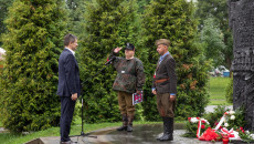 Jacek Włosowicz stoi obok dwóch członków grupy rekonstrukcyjnej w powstańczych strojach, jeden z nich salutuje